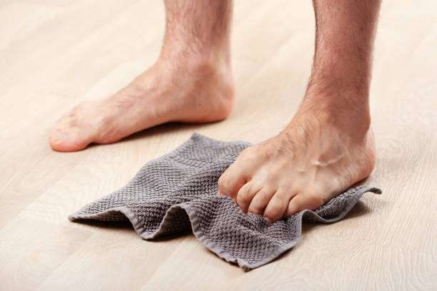 man grabbing gray towel off floor using toes